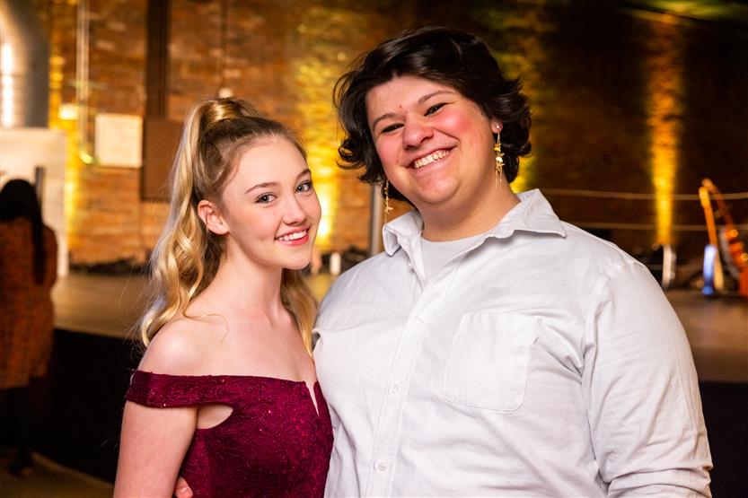 A woman wearing a red dress smiles with a woman wearing a white shirt